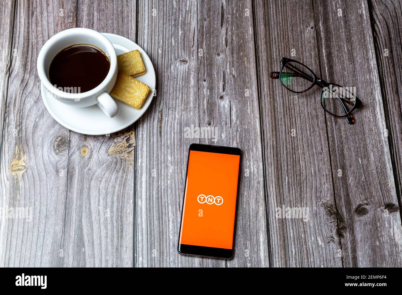 Un téléphone portable ou un téléphone portable sur une table en bois Avec l'application de livraison TNT ouverte à côté d'un café et lunettes Banque D'Images