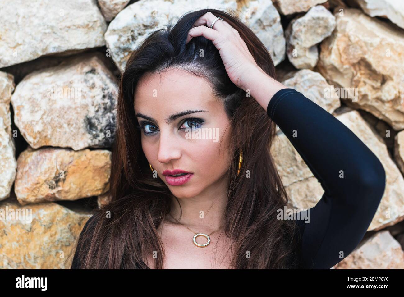 Magnifique fille posant sur le mur de pierre avec sa main tirant Ses cheveux Banque D'Images