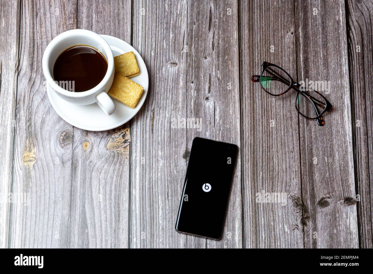 Un téléphone portable ou un téléphone portable sur une table en bois Avec l'application Beats ouverte à côté d'un café et lunettes Banque D'Images