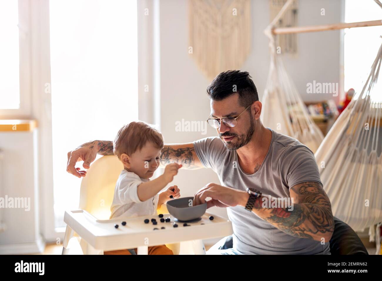 Un père qui allaite son bébé qui est assis dans un chaise haute Banque D'Images