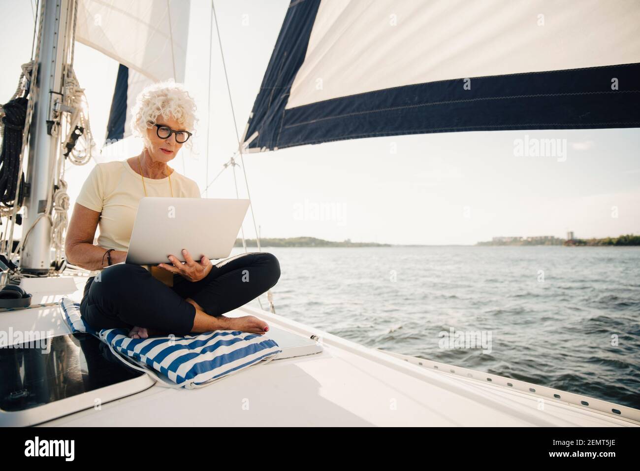 Femme sénior travaillant à distance en voilier par beau temps Banque D'Images