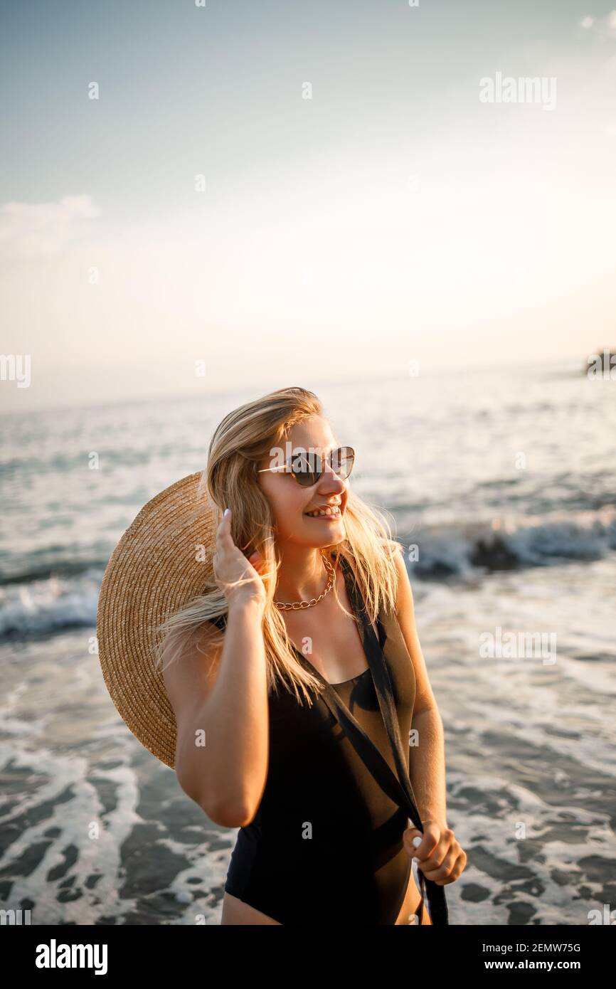 Jeune belle femme dans un maillot de bain noir et chapeau avec des lunettes  marche le long de la plage en Turquie au coucher du soleil. Le concept de  la récréation de