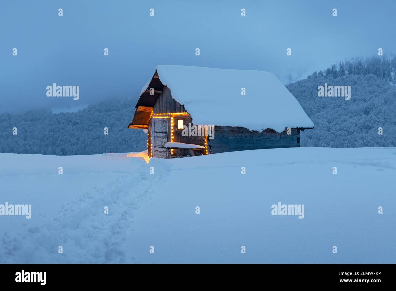 Paysage d'hiver fantastique avec cabine en bois lumineux dans une forêt enneigée. Maison confortable dans les montagnes de Carpathian. Concept de vacances de Noël Banque D'Images