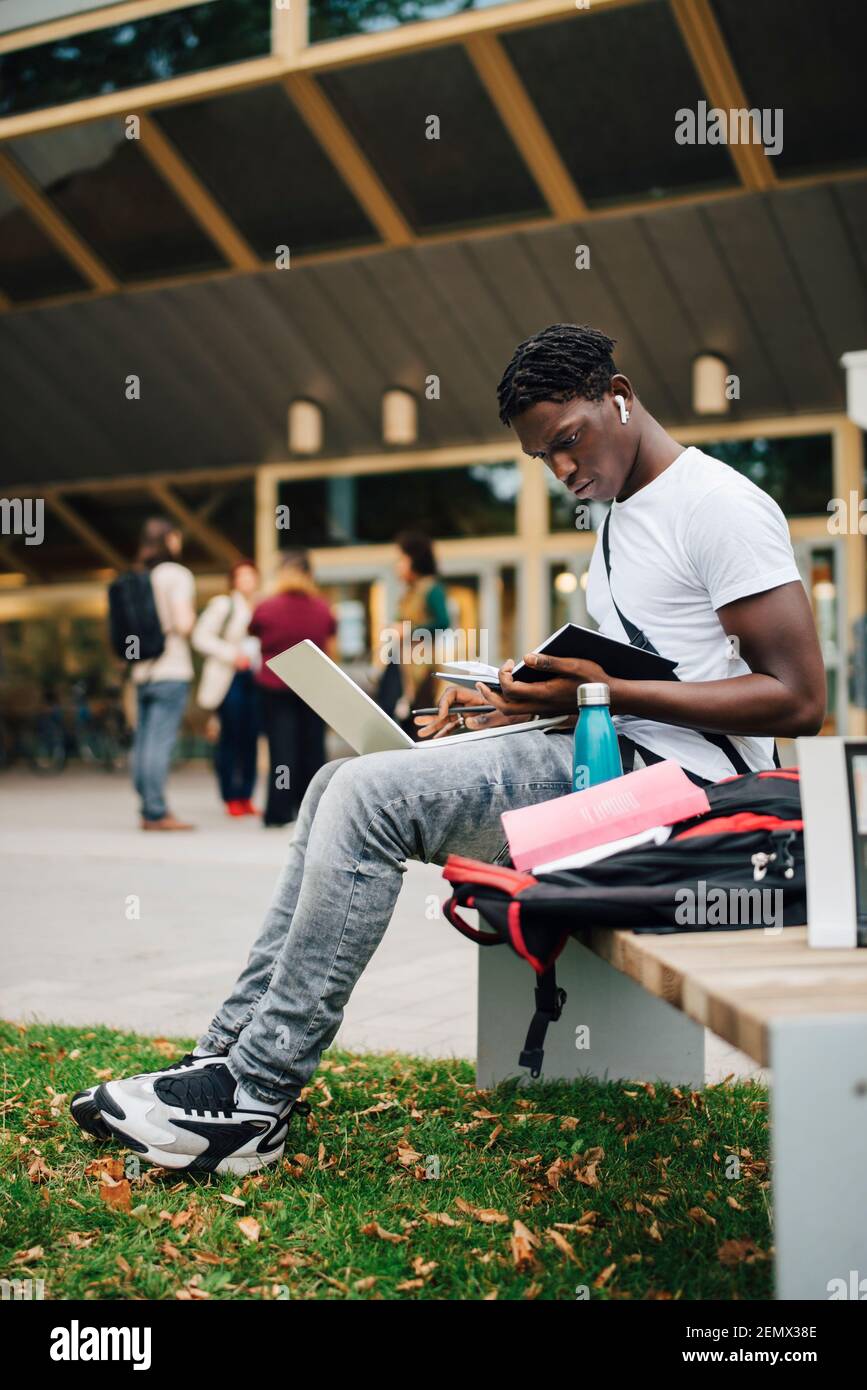 Un étudiant africain en train de lire un livre tout en étant assis sur le banc campus universitaire Banque D'Images