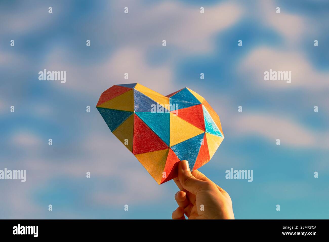 Les mains des enfants tiennent le coeur coloré sur fond bleu ciel. Concept de journée mondiale de sensibilisation à l'autisme Banque D'Images