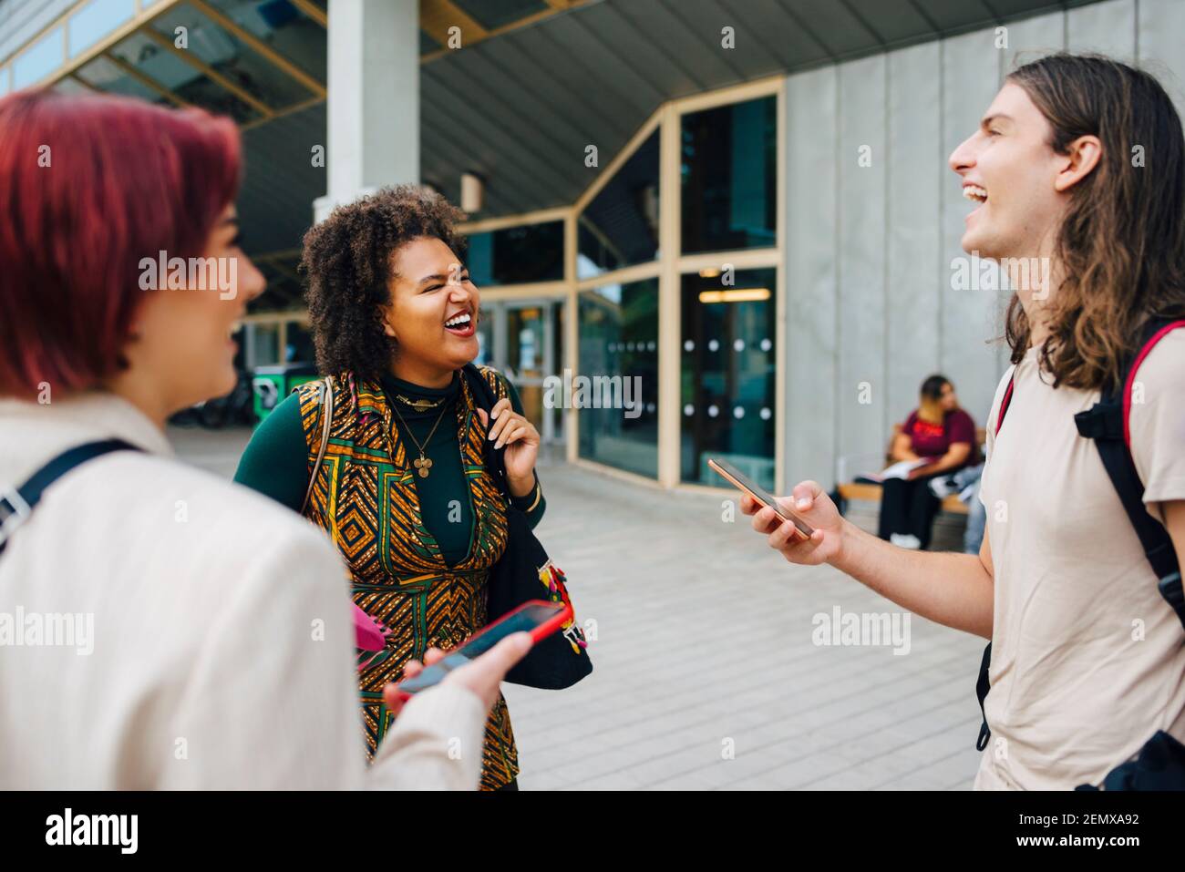 Les jeunes étudiants de l'université rient tout en parlant les uns avec les autres à campus universitaire Banque D'Images