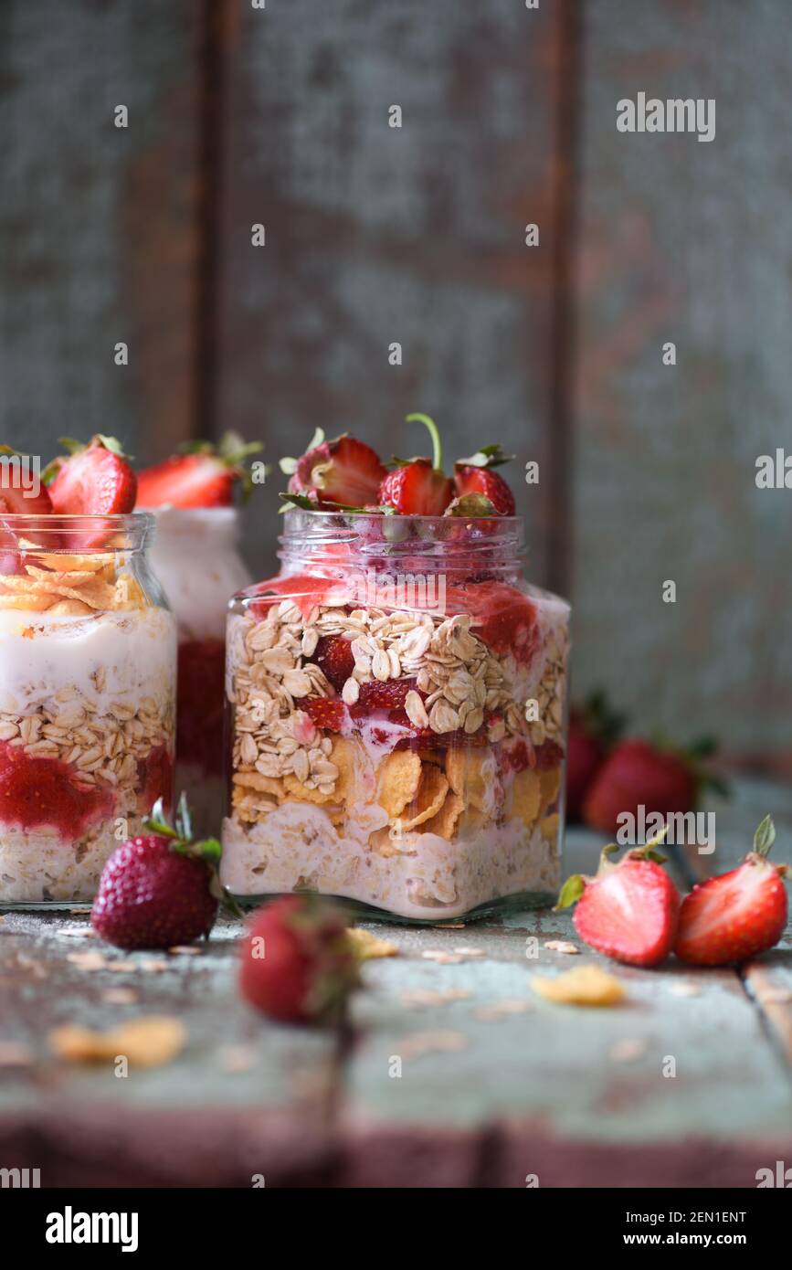 Petit déjeuner sain sans gluten, pauvre en calories. Avoine de nuit avec fraise biologique et flocons de maïs dans des pots de verre sur fond bleu shabby copyspace ver Banque D'Images