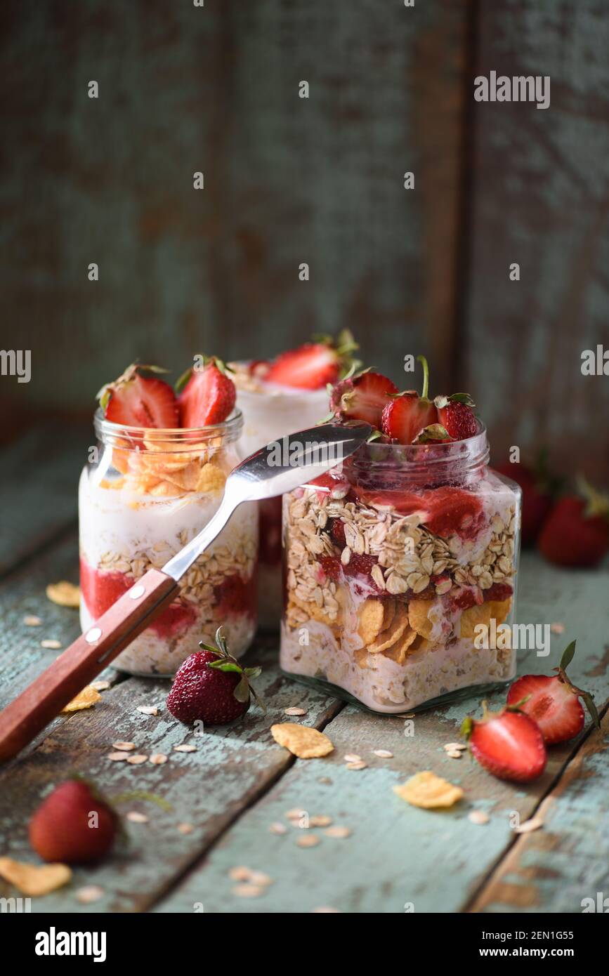 Petit déjeuner sain d'été. Avoine de nuit avec fraise et flocons de maïs dans des pots en verre sur fond bleu de merde copyspace vertical Banque D'Images