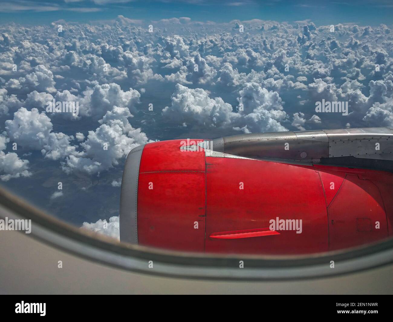 Découvrez une fenêtre d'avion d'un moteur rouge très lumineux et de nombreux nuages bosselés qui remplissent l'horizon. Banque D'Images