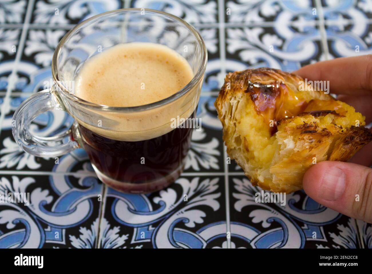 Main tenant une tarte à la crème portugaise appelée pastel de nata, avec un café espresso noir Banque D'Images