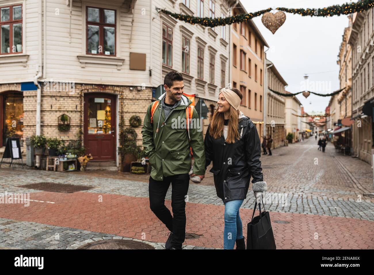 Couple souriant tenant les mains tout en marchant dans la rue en ville Banque D'Images