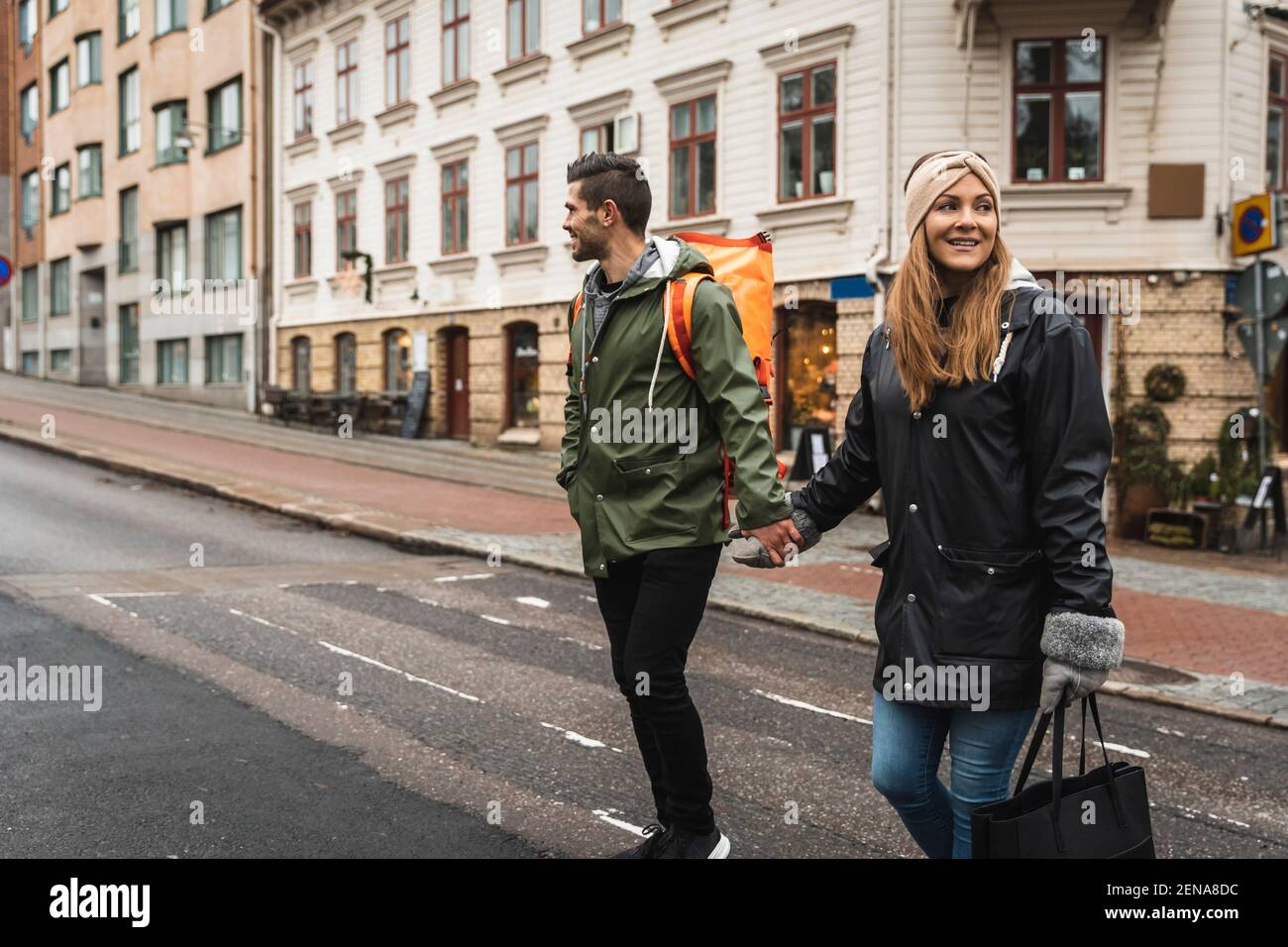 Couple souriant tenant les mains en traversant la rue en ville Banque D'Images