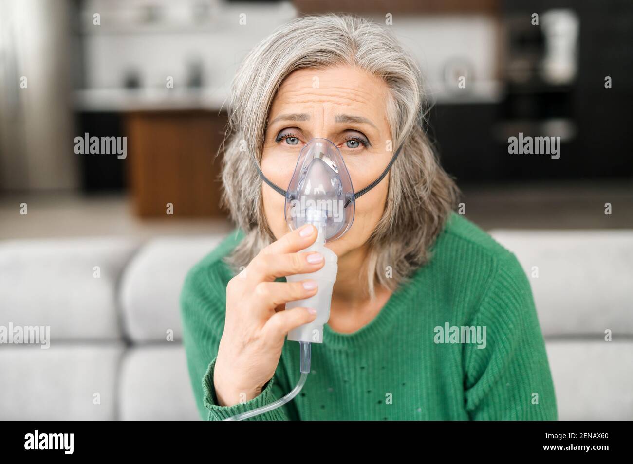Femme âgée cheveux gris, a beaucoup de rides, se sent mal, tenant le masque d'oxygène, manque d'oxygène, sensible à l'air pollué, assis à la maison sur un auto-isolement, semble malade, faisant l'inhalation Banque D'Images