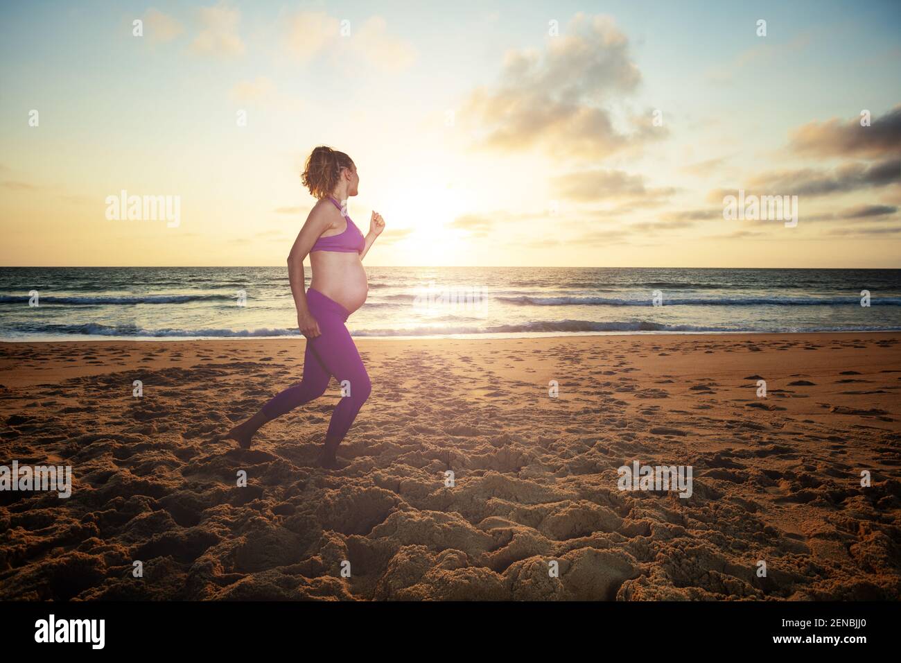 Femme enceinte qui fait du jogging sur la plage au coucher du soleil Banque D'Images