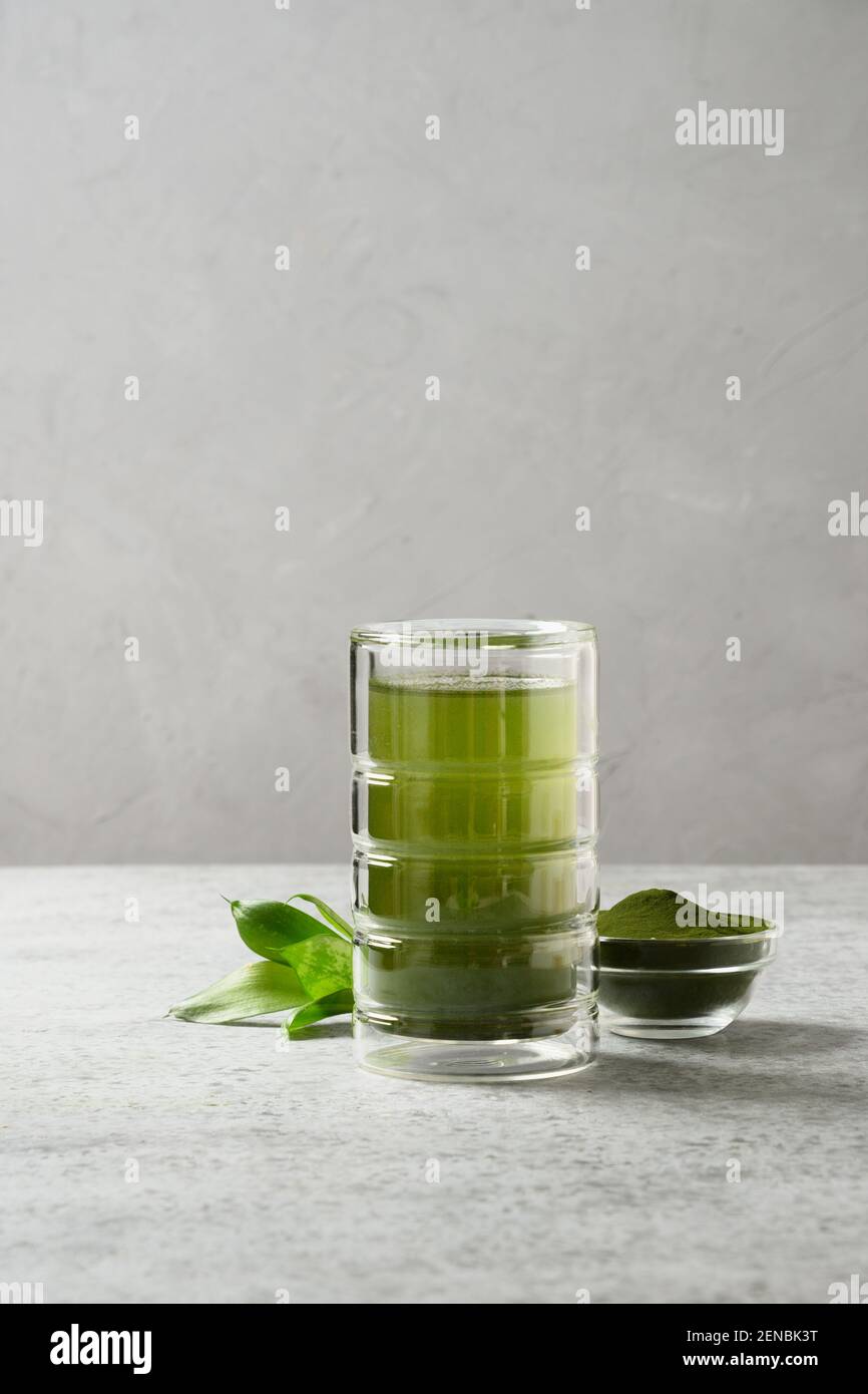 Chlorella detox boire dans le verre et la poudre dans un bol sur un fond gris. Format vertical. Banque D'Images