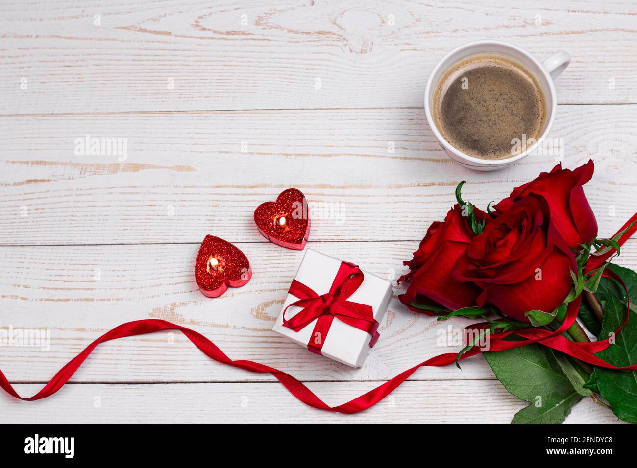 Saint-Valentin romantique petit déjeuner plat fond. Tasse de café bougies en forme de coeur avec boîte cadeau et roses rouges sur fond blanc en bois. Banque D'Images