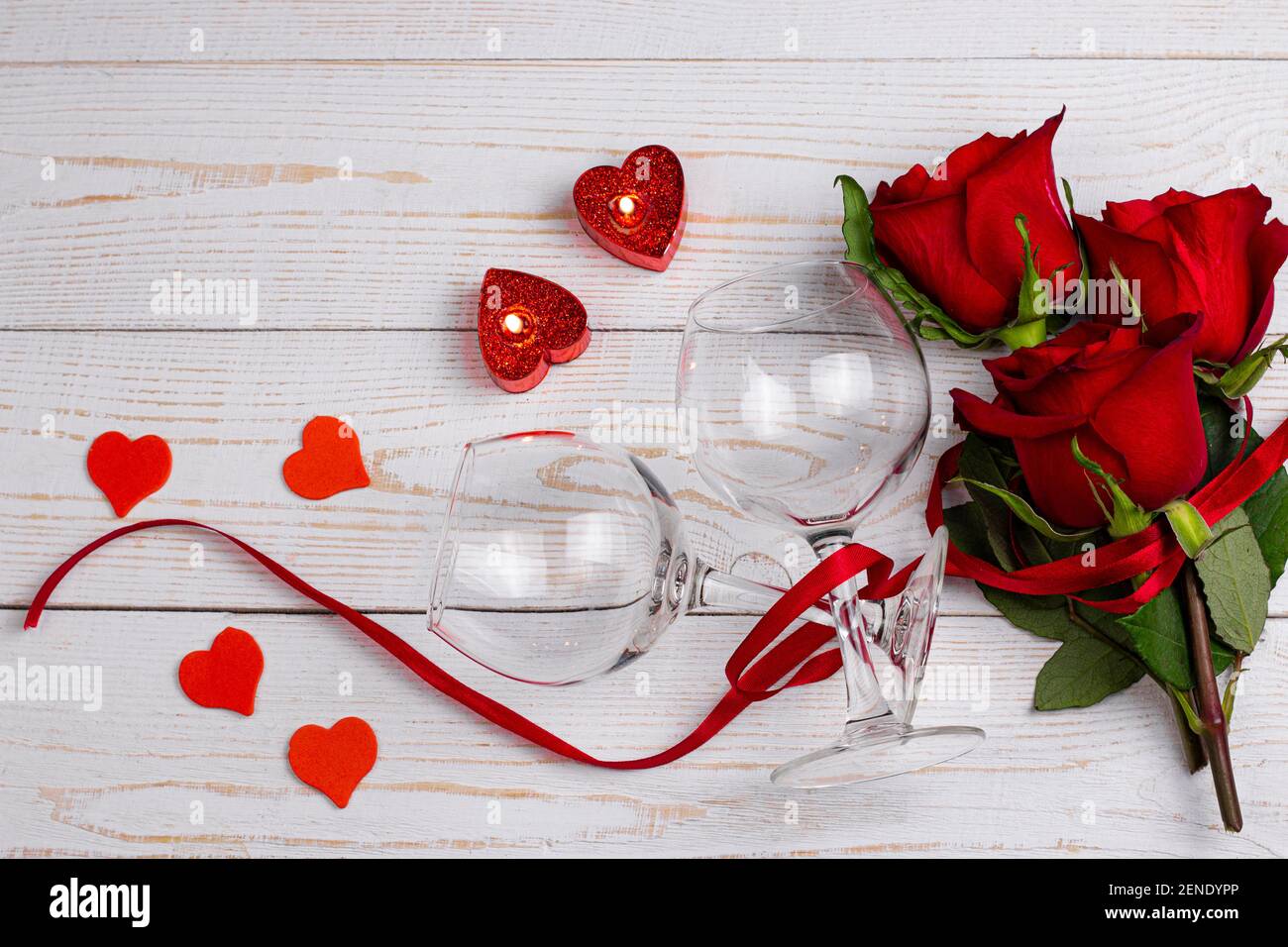 Verres à vin, bougies, roses rouges avec ruban rouge et petit coeur sur fond blanc en bois. Saint-Valentin dîner romantique plat Lay Top View concept Banque D'Images