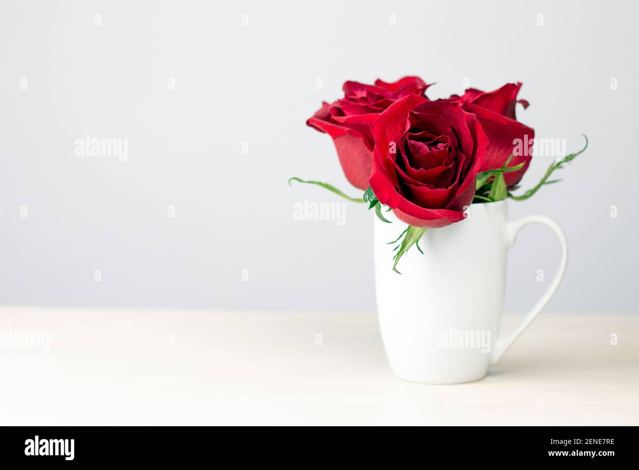 Bouquet de roses rouges dans une tasse blanche sur fond de bois. Carte cadeau de Saint-Valentin avec espace pour les copies. Banque D'Images