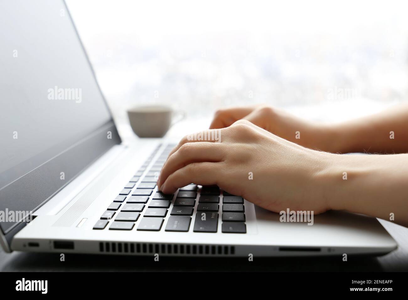 Femme travaille à l'ordinateur portable sur fond de fenêtre. Les femmes ont les mains sur le clavier en plein soleil Banque D'Images