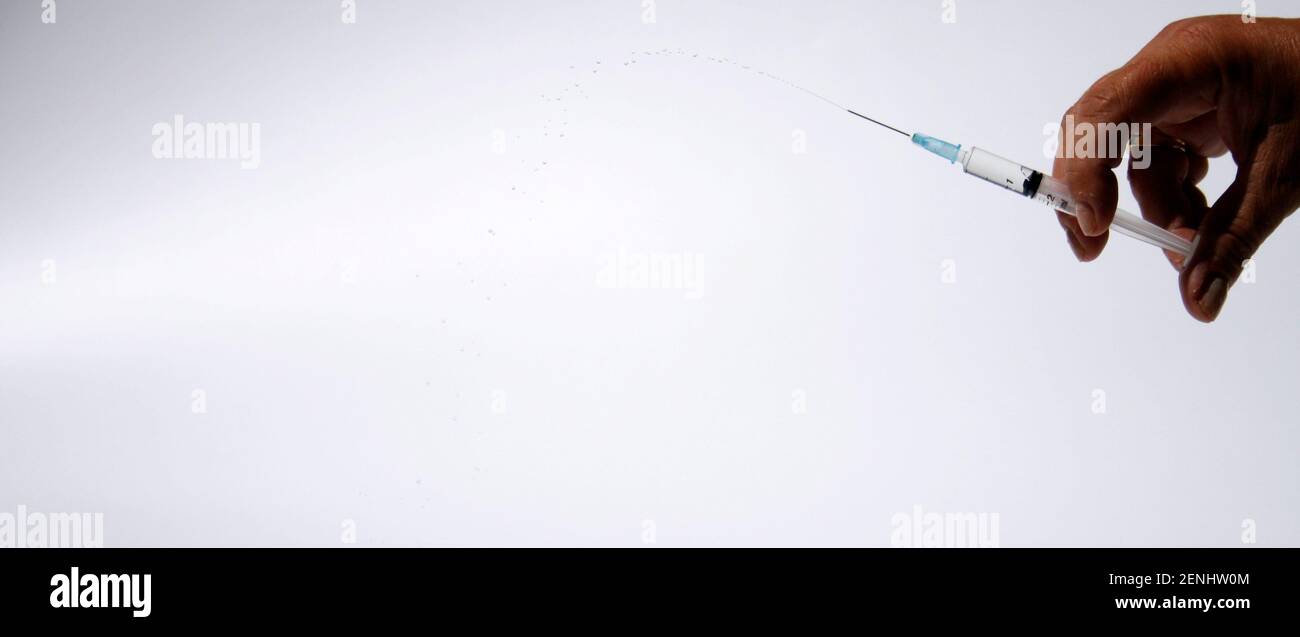 Main isolée avec seringue et gouttes filés dans l'air. Beaucoup d'espace de copie sur le côté gauche Banque D'Images