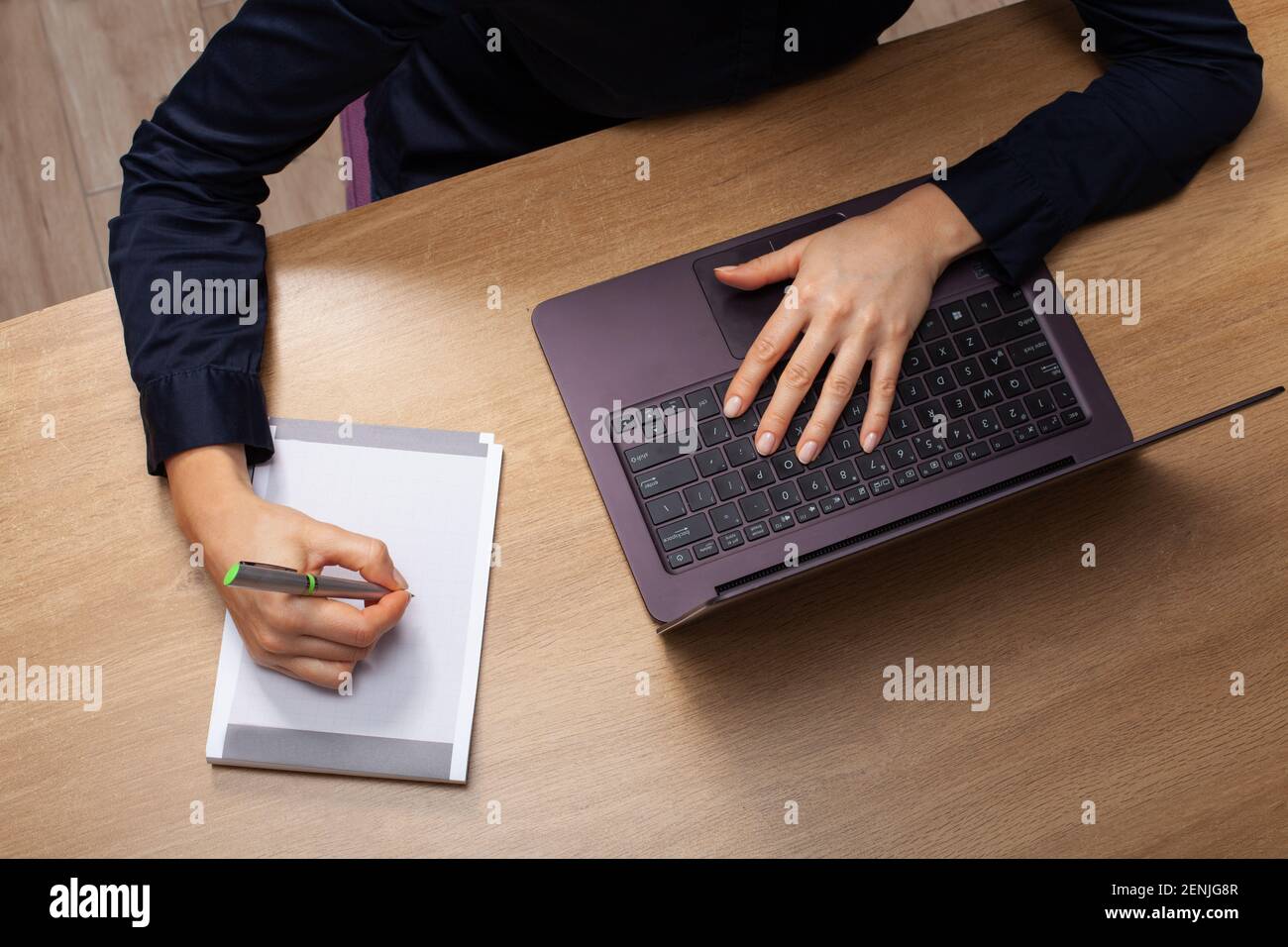 Vue détaillée d'une femme à la maison assise à la table avec un ordinateur portable, prenant des notes dans un ordinateur portable. Vêtu d'une chemise noire. Banque D'Images