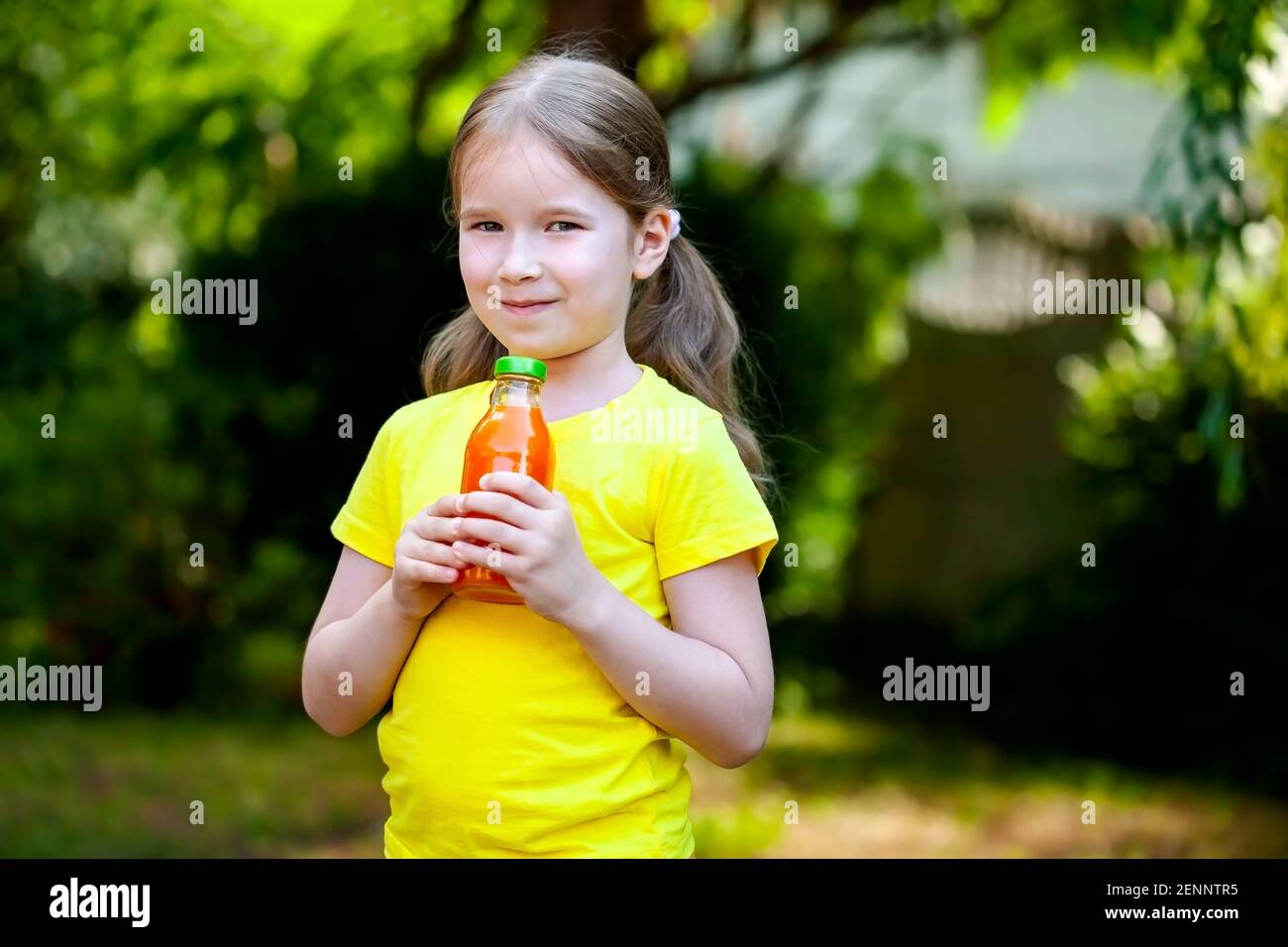 Jeune enfant heureux, une petite fille seule tenant une bouteille de jus de carotte d'orange sain souriant, plein air portrait de parc, espace de copie flou backgroun Banque D'Images