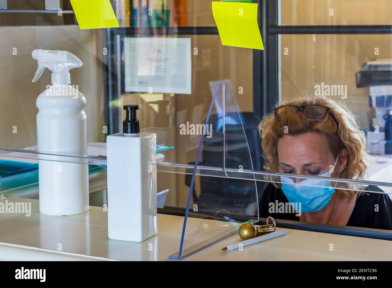 Une femme avec un masque de protection travaille dans un bureau à la réception d'un hôtel séparé par une feuille de plexiglas Banque D'Images