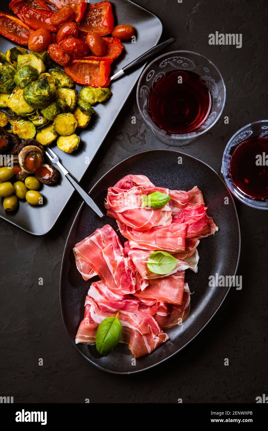 Prosciutto avec différents hors-d'œuvre avec un verre de vin rouge sur fond noir. Sur les légumes rôtis, en-cas sain Banque D'Images