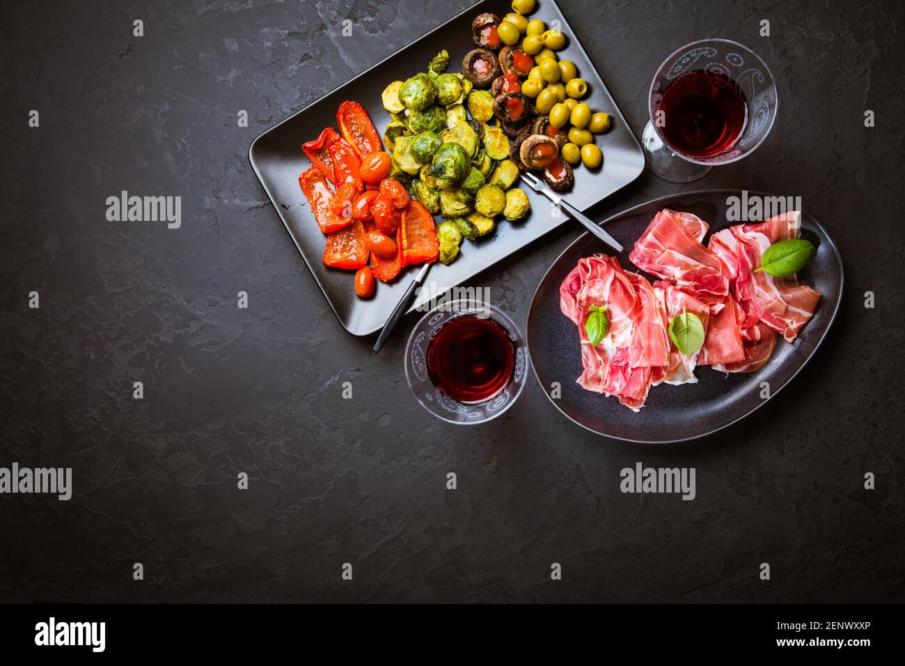 Prosciutto avec différents hors-d'œuvre avec un verre de vin rouge sur fond noir. Sur les légumes rôtis, en-cas sain Banque D'Images