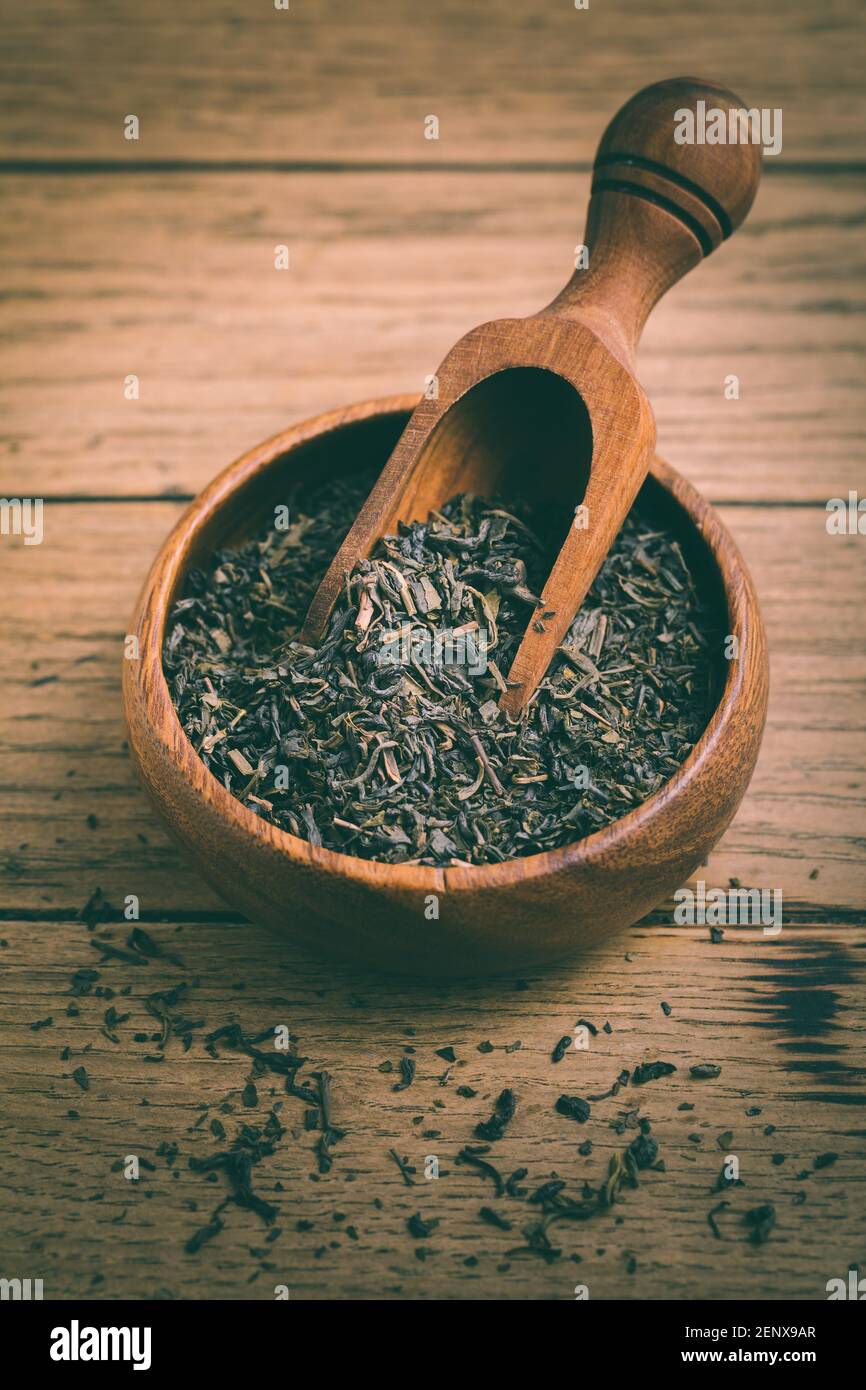 Feuilles de thé noir séchées dans un bol sur fond de bois Banque D'Images