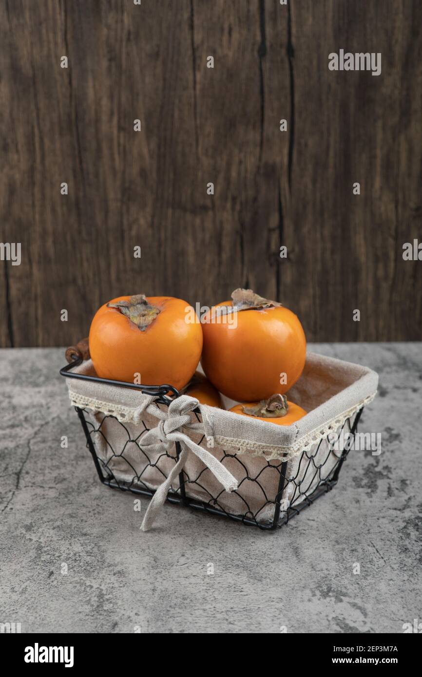 De délicieux fruits fuyu persimmon placés dans un panier sur une surface en marbre Banque D'Images