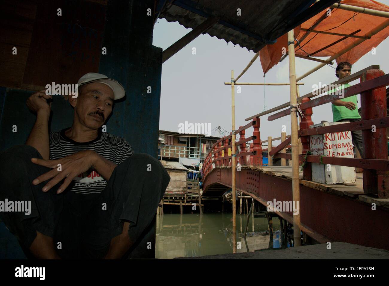 Portrait d'un homme comme il se détend à côté d'un pont sur un village populairement connu sous le nom de Luar Batang, sur l'estuaire de la rivière Ciliwung, près du port traditionnel de Sunda Kelapa dans la zone côtière de Jakarta, Indonésie (2008). Banque D'Images