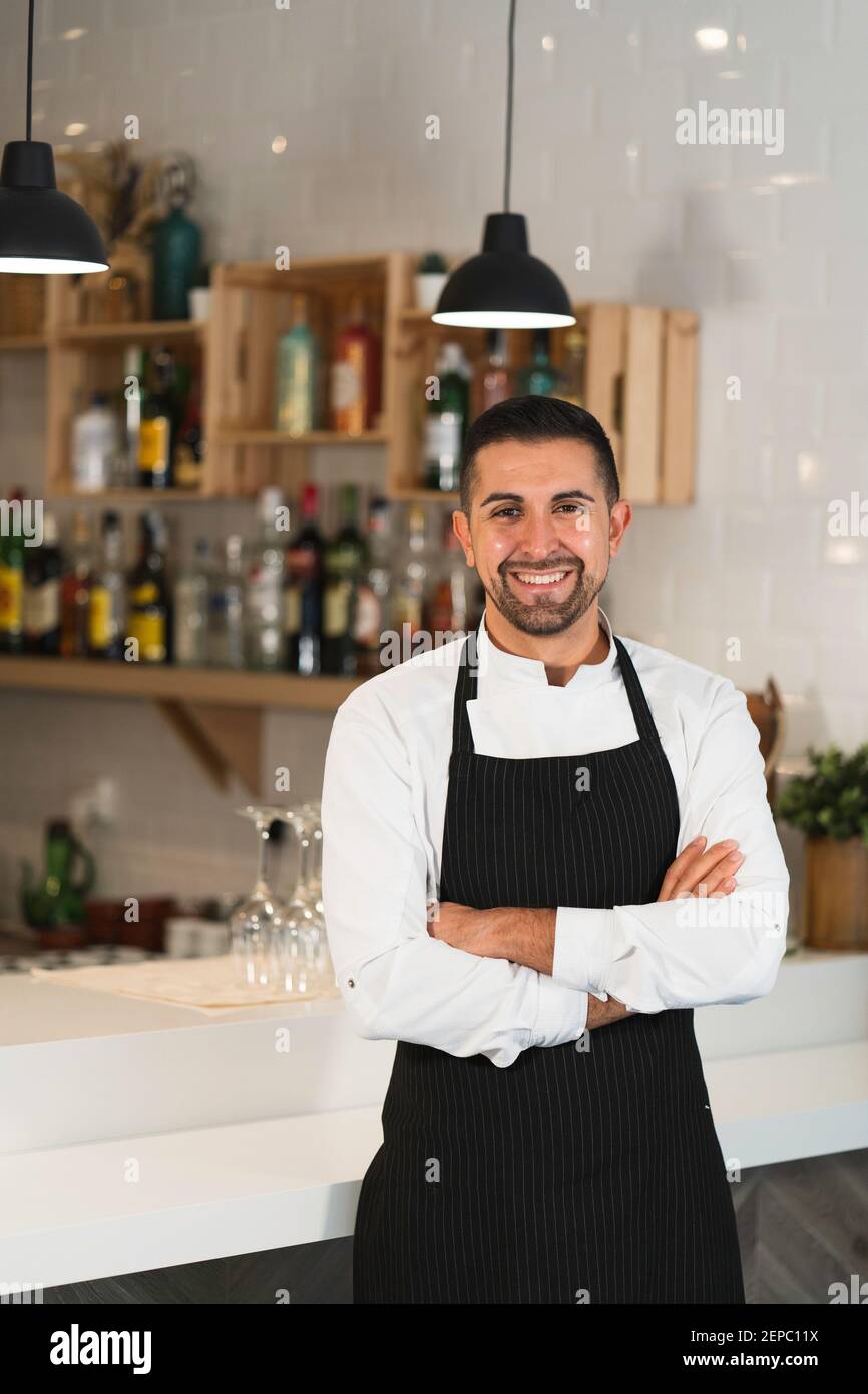 Portrait d'un jeune chef heureux posant portant l'uniforme et robe de cuisine dans le restaurant Banque D'Images