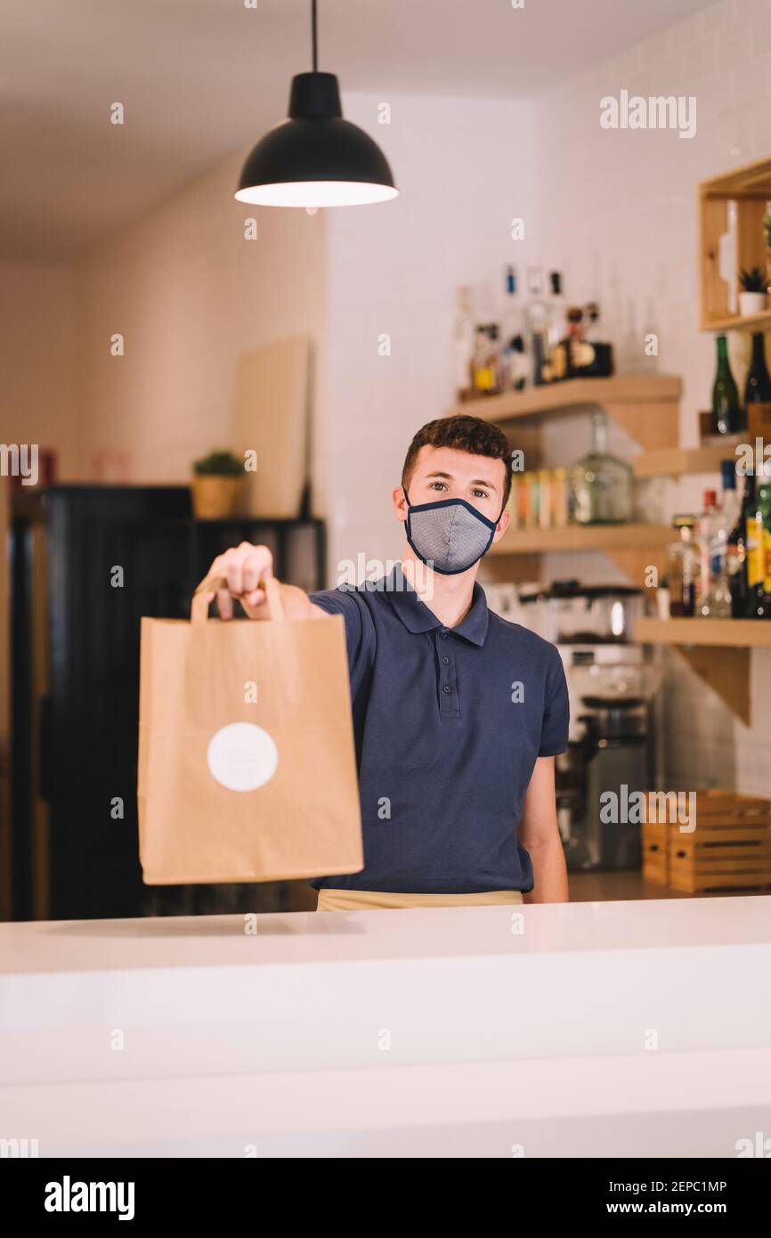 portrait d'un serveur professionnel avec masque qui livre un sac en papier recyclé avec une commande à emporter dans un restaurant pendant une pandémie de coronavirus. Banque D'Images