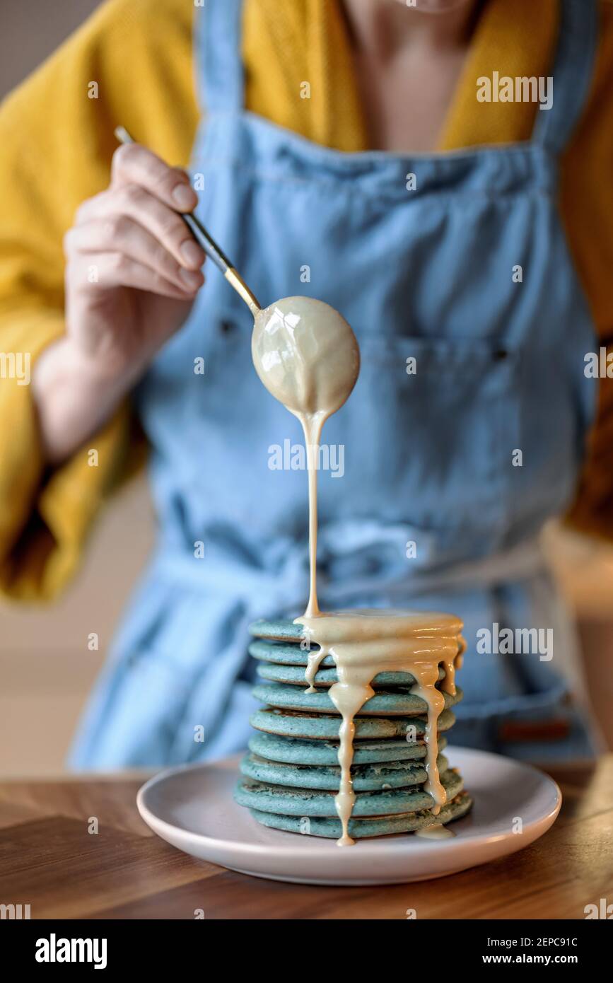 Femme versant des crêpes bleues avec une souse au caramel. Banque D'Images