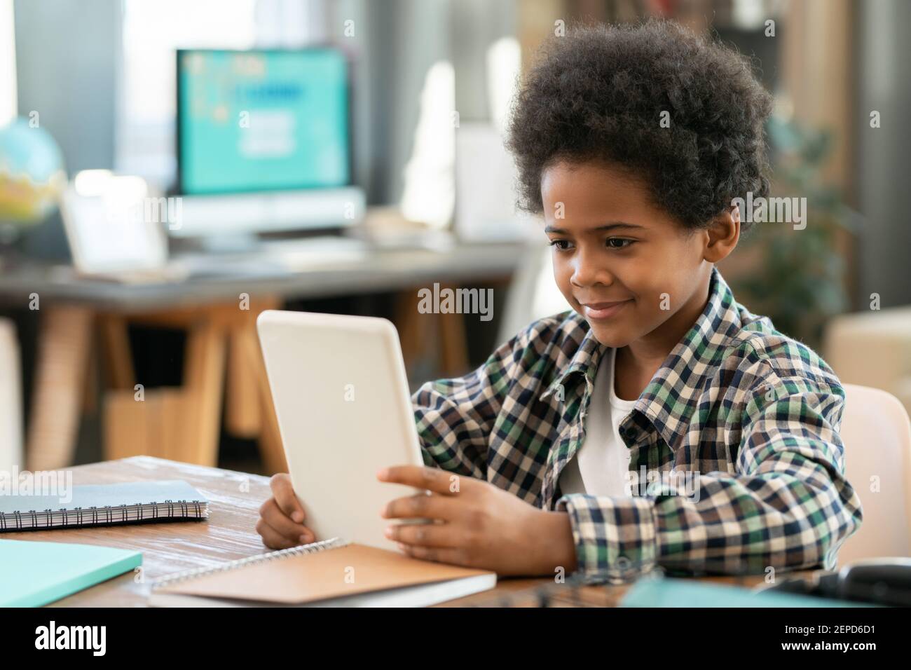 Adorable élève d'origine africaine assis à table avant de l'appareil photo dans le salon et regarder des vidéos éducatives en ligne Banque D'Images