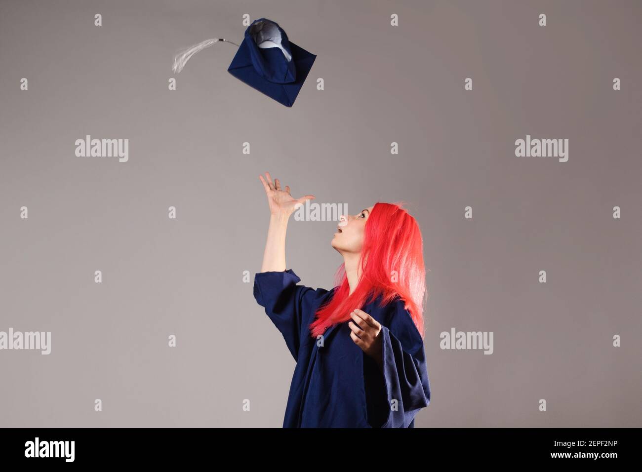 Bon diplômé sur fond gris. Une jeune femme aux cheveux brillants avec une casquette et une robe. Jetez le capuchon. Banque D'Images