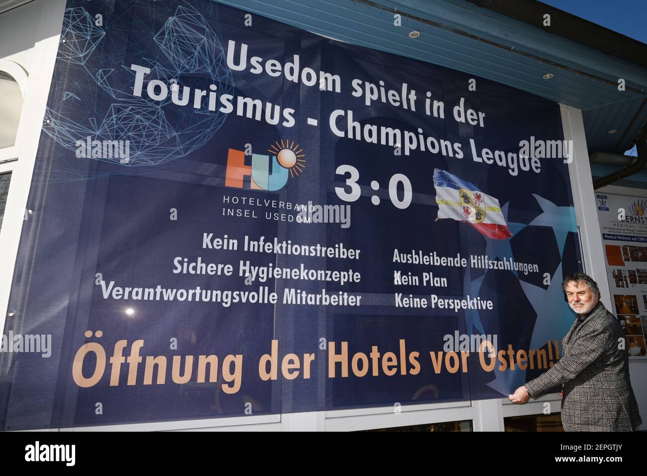 Koserow, Allemagne. 27 février 2021. Michael Raffelt, exploitant hôtelier de la Hanse-Kogge, se dresse à Koserow devant une affiche avec les mots « ouverture des hôtels avant Pâques ». Sur l'île d'Usedom, un producteur de vacances, les hôteliers ont lancé une campagne d'affiches le même jour, soulignant les conséquences imminentes de mois de fermetures forcées. Credit: Stefan Sauer/dpa/Alay Live News Banque D'Images