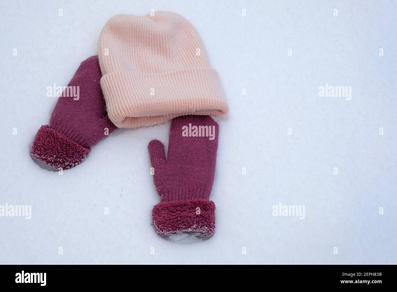 Bonnet et moufles en tricot rose avec vue sur le haut de la neige blanche. Vêtements chauds pour l'hiver. Banque D'Images