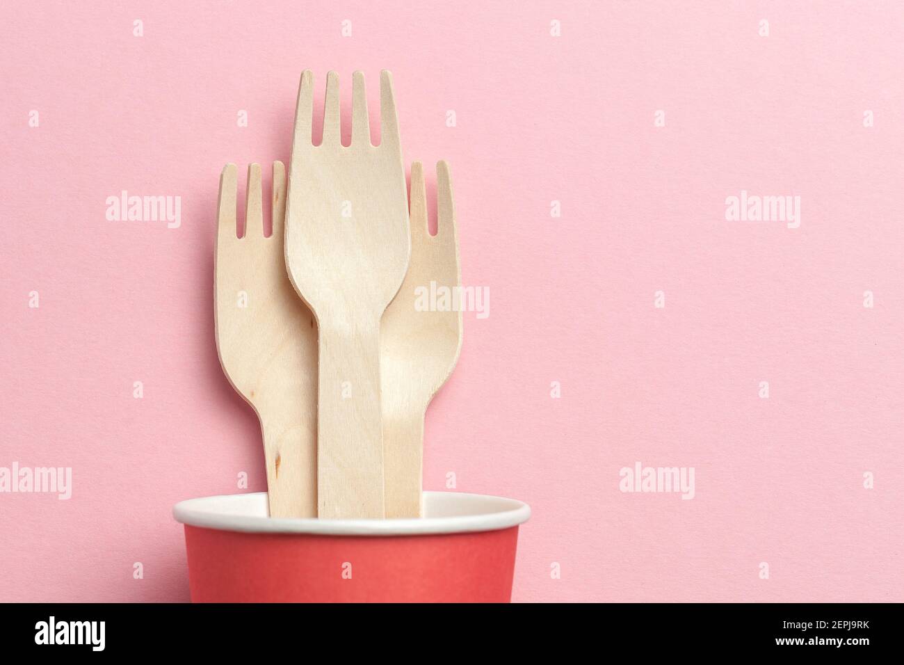 ustensiles de cuisine écologiques et jetables. fourchettes en bois dans une tasse en papier sur fond de corail rose. pose à plat. espace pour copier Banque D'Images