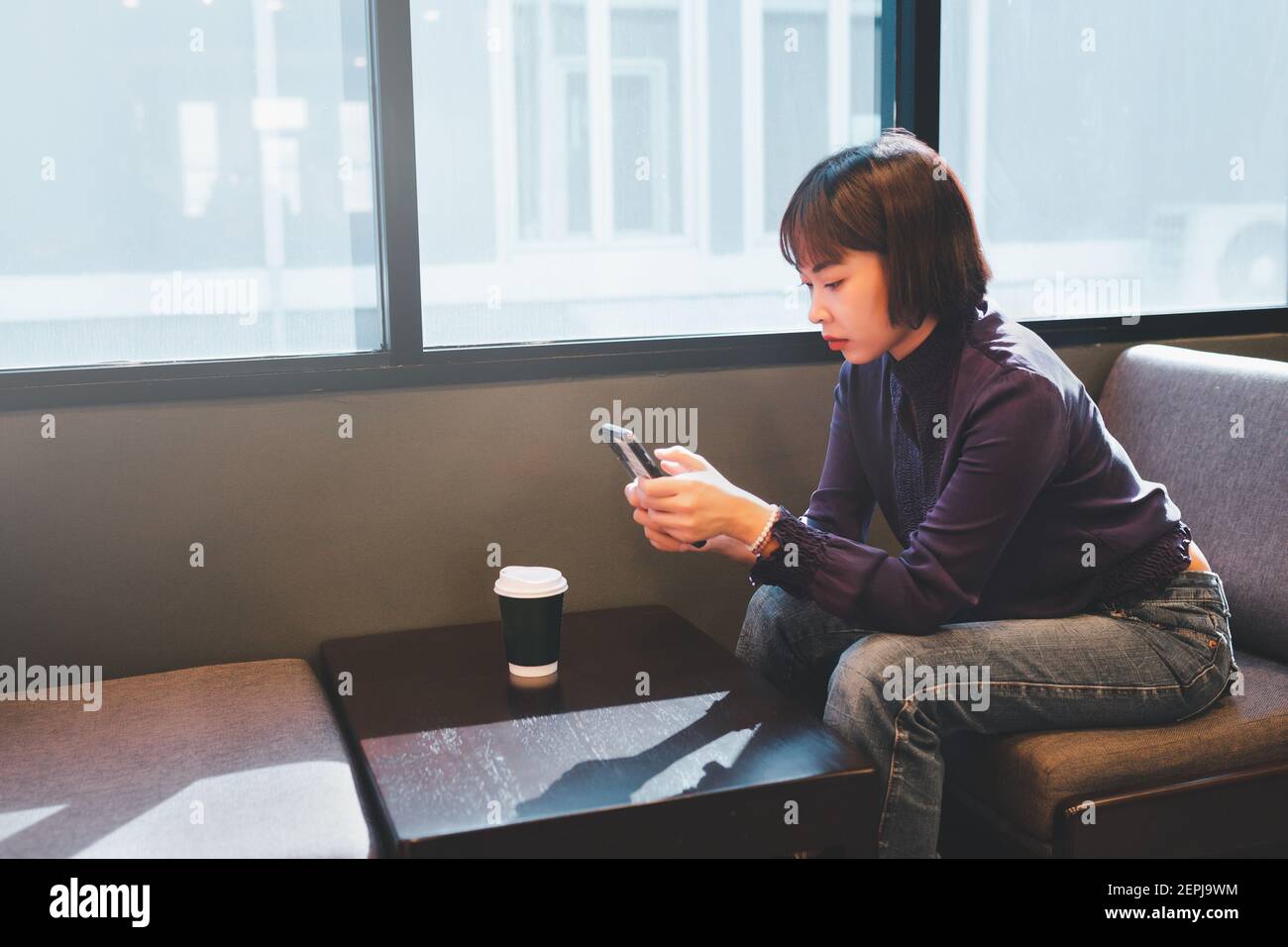 Jeune femme asiatique utilisant un téléphone portable au café avec une tasse de café. Banque D'Images Jeune femme asiatique utilisant un téléphone portable au café avec une tasse de café. Banque D'Images
