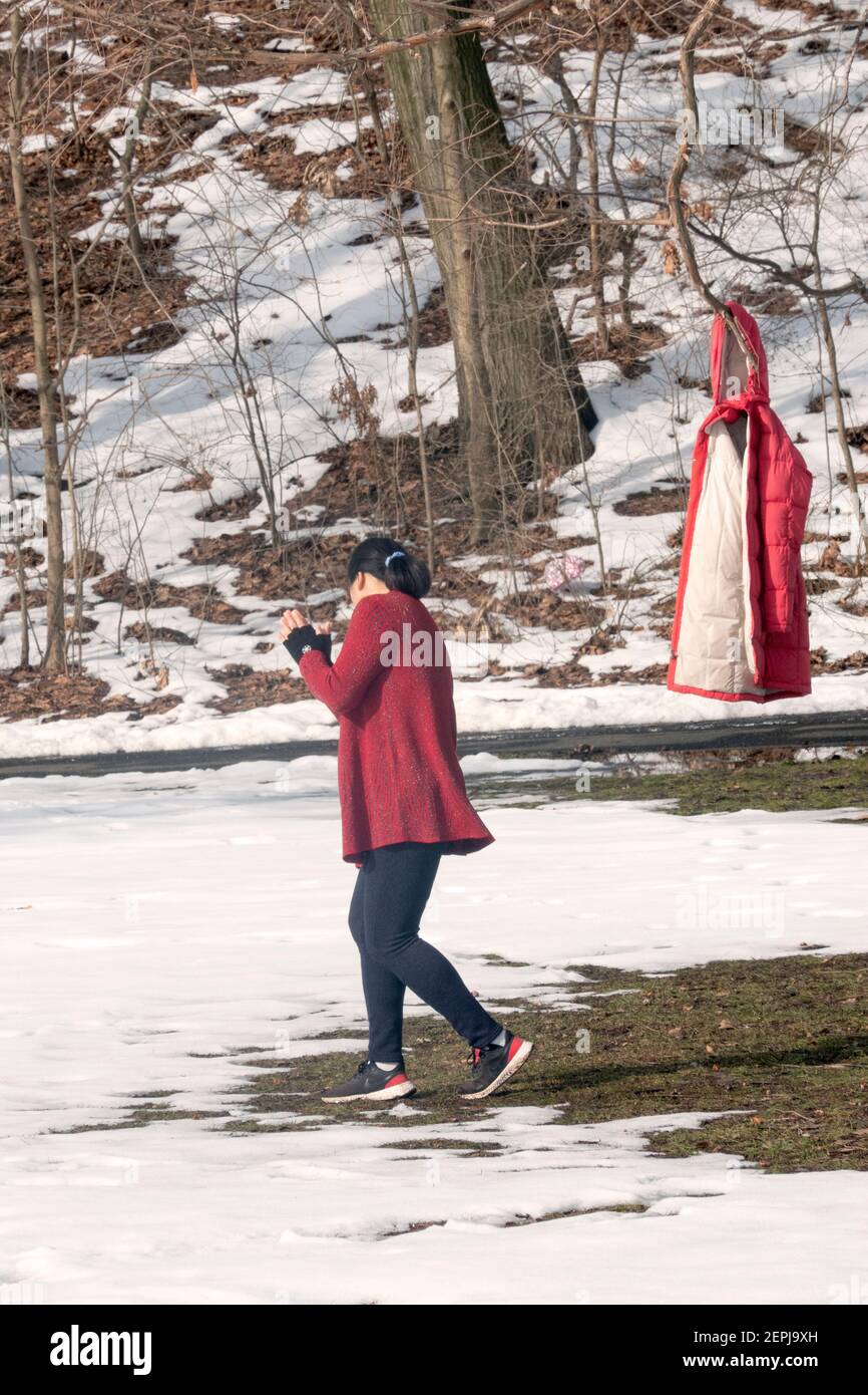 Par temps froid d'hiver, une femme asiatique américaine à un cours d'exercice de danse se réchauffe et porte sa veste sur un arbre. À Flushing, Queens, New York. Banque D'Images