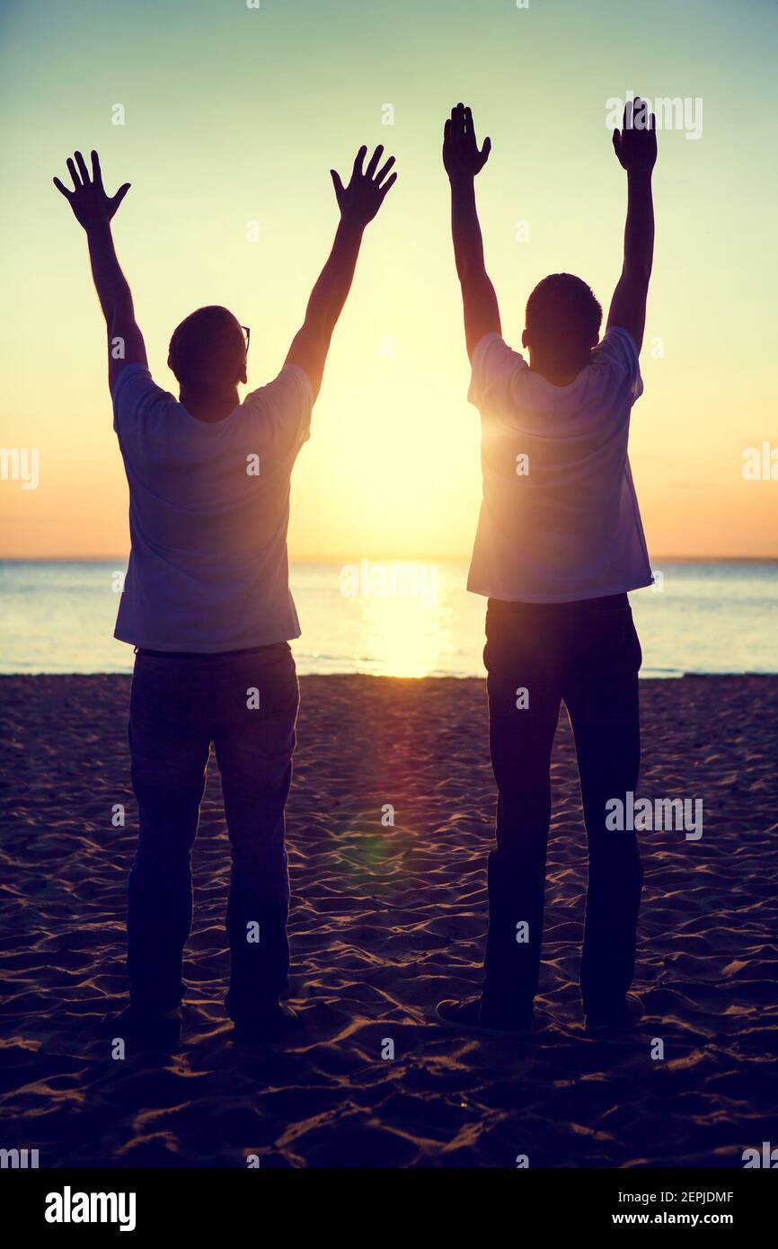 Ton de la silhouette de deux hommes avec les mains vers le haut à L'arrière-plan du coucher du soleil Banque D'Images