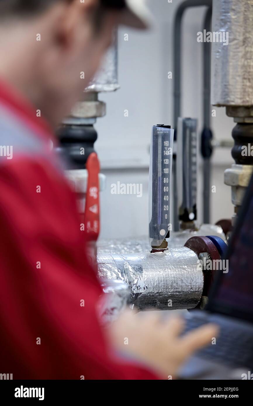 Industrie de l'énergie. Un technicien vêtu de combinaisons rouges et un casque blanc vérifiant les paramètres de chauffage. Technologie de distribution de l'eau de chauffage. Service Banque D'Images