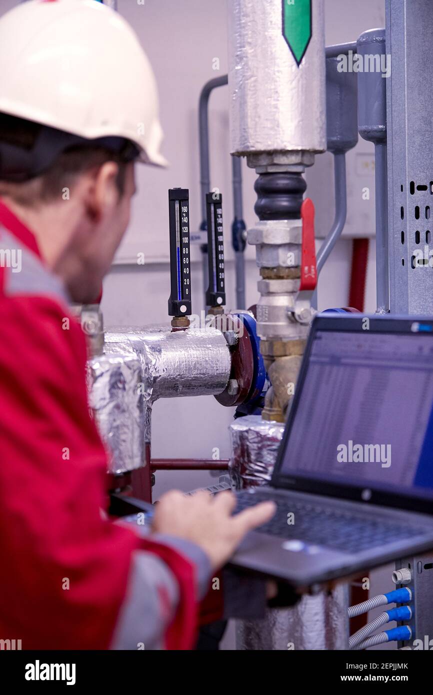 Industrie de l'énergie. Un technicien vêtu de combinaisons rouges et un casque blanc vérifiant les paramètres de chauffage. Technologie de distribution de l'eau de chauffage. Service Banque D'Images