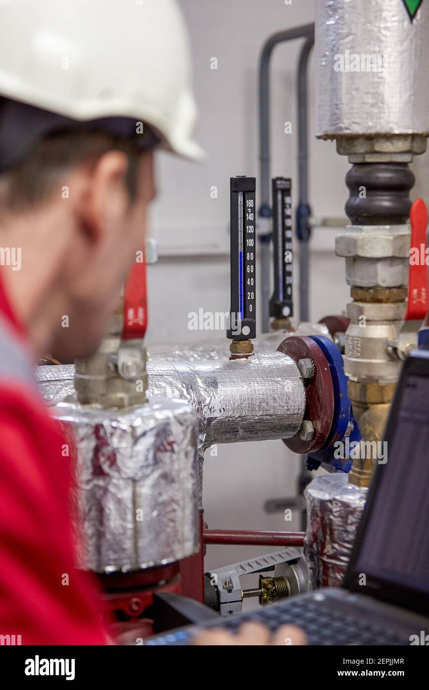 Industrie de l'énergie. Un technicien vêtu de combinaisons rouges et un casque blanc vérifiant les paramètres de chauffage. Technologie de distribution de l'eau de chauffage. Service Banque D'Images