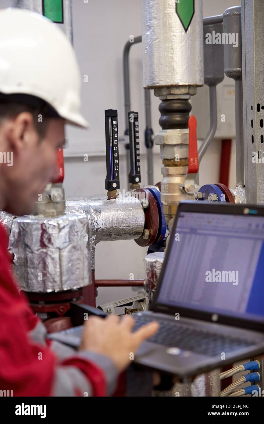 Industrie de l'énergie. Un technicien vêtu de combinaisons rouges et un casque blanc vérifiant les paramètres de chauffage. Technologie de distribution de l'eau de chauffage. Service Banque D'Images