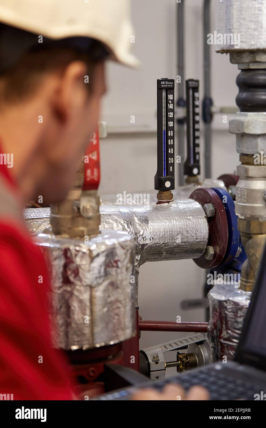 Industrie de l'énergie. Un technicien vêtu de combinaisons rouges et un casque blanc vérifiant les paramètres de chauffage. Technologie de distribution de l'eau de chauffage. Service Banque D'Images
