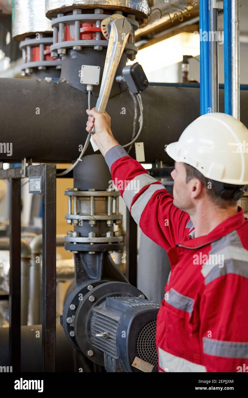 Industrie de l'énergie. Un technicien vêtu d'une salopette rouge et d'un casque blanc vérifiant les paramètres de chauffage. Technologie de chauffage. Banque D'Images