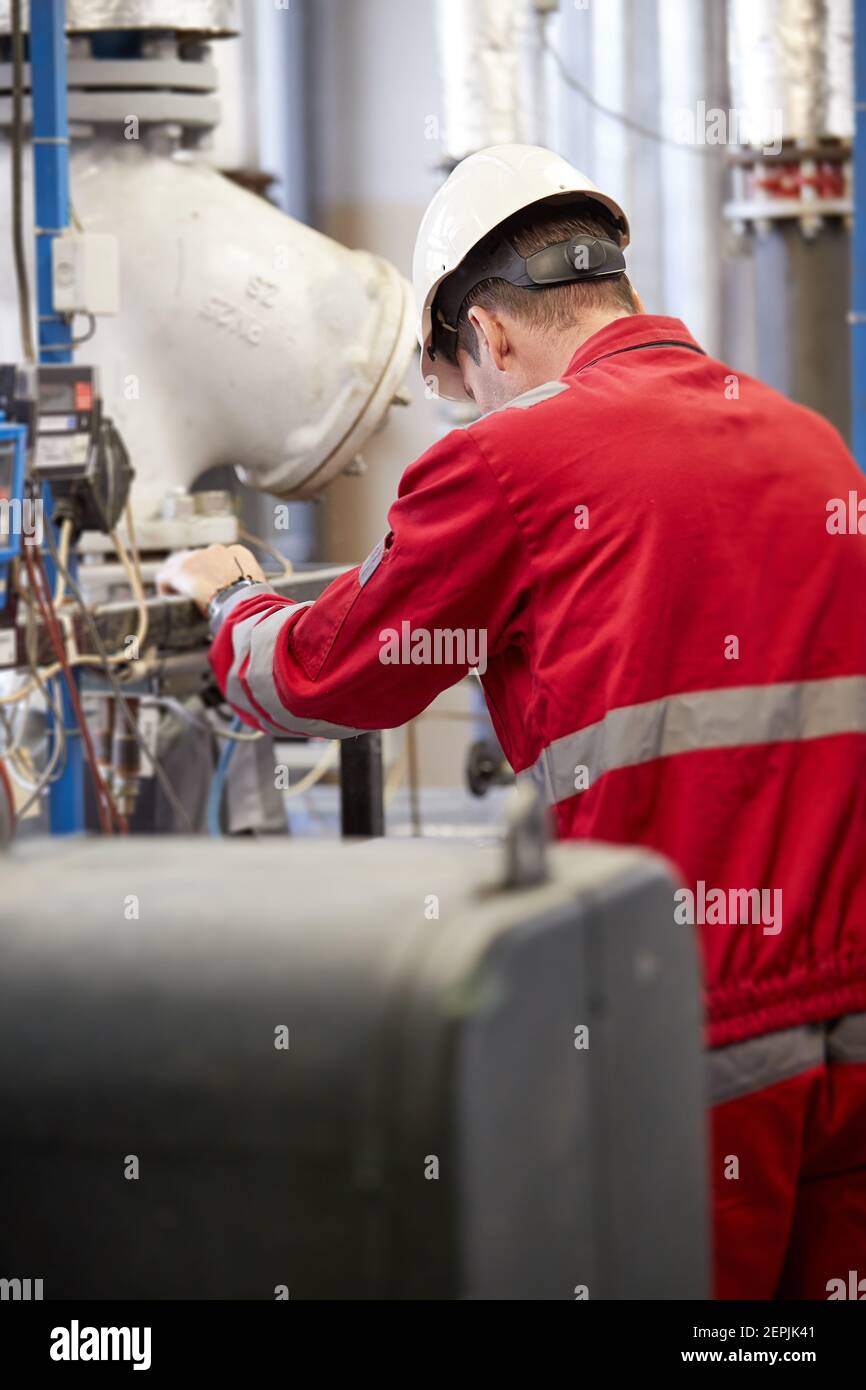 Industrie de l'énergie. Un technicien vêtu d'une combinaison rouge et d'un casque blanc vérifiant les paramètres de chauffage. Technologie de distribution d'eau de chauffage. Banque D'Images